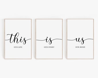 May include: Three white framed prints with black calligraphy. The first print says "this" with the words "our life" underneath. The second print says "is" with the words "our story" underneath. The third print says "us" with the words "our home" underneath.