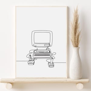 Puede incluir: Un dibujo en blanco y negro de una computadora vintage con dos joysticks. El dibujo está enmarcado y se muestra en un estante con un jarrón de hierba de la pampa seca.