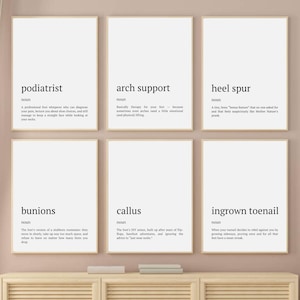 May include: Six framed prints with black text on white backgrounds. The prints feature humorous definitions for podiatrist, arch support, heel spur, bunions, callus, and ingrown toenail. The frames are a light brown colour.