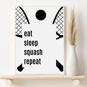 Op de afbeelding: Zwart-witte print met een squashracket en een bal, en de tekst "eat sleep squash repeat".