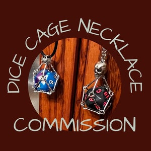 Puede incluir: Dos collares de jaula plateada con dados en su interior. Un dado es azul con números blancos y el otro es negro con números rosas. Los collares cuelgan de una superficie de madera. El texto "Dice Cage Necklace Commission" está escrito en un círculo alrededor de los collares.