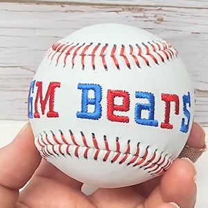 May include: White baseball with red and blue embroidered text that reads "GM Bears".