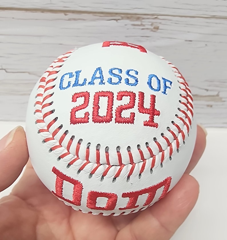 May include: White baseball with red stitching and red embroidered text that says "Class of 2024" and "DOTT"