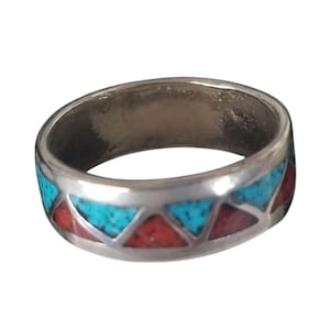 May include: A silver band ring featuring a geometric inlay pattern of alternating triangular segments. The design consists of bright turquoise blue and deep red stone inlays set within the polished metal surface of the circular ring band.