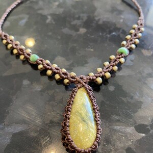 May include: A brown macrame necklace with a teardrop-shaped yellow stone pendant and green beads.