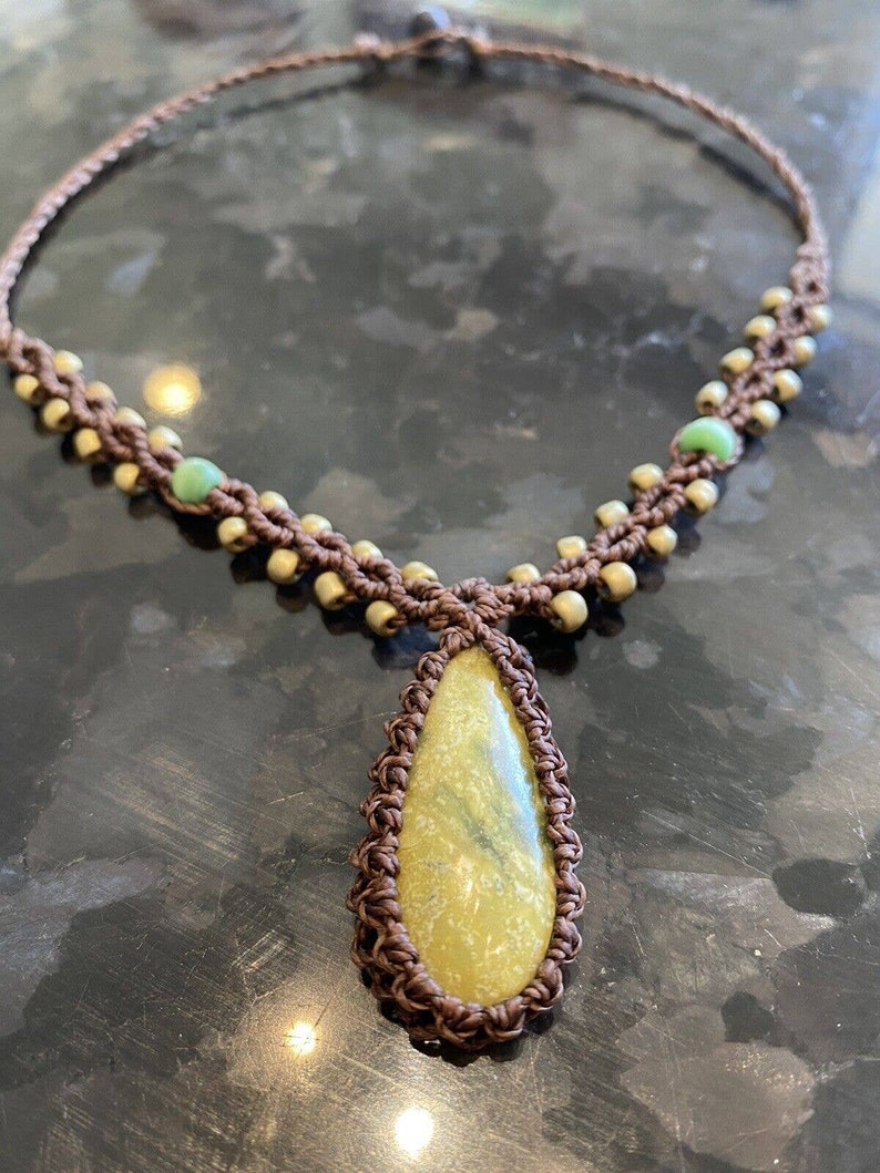 May include: A brown macrame necklace with a teardrop-shaped yellow stone pendant and green beads.