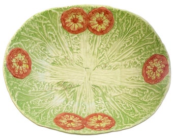 May include: A large, oval-shaped serving bowl with a green and white cabbage design. The bowl has five red tomato slices around the rim.