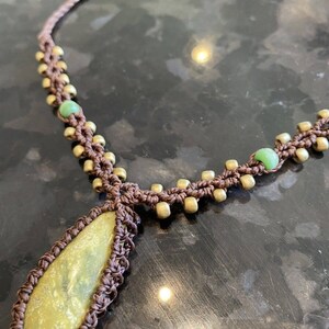 May include: A brown macrame necklace with a teardrop-shaped green stone pendant and gold beads.