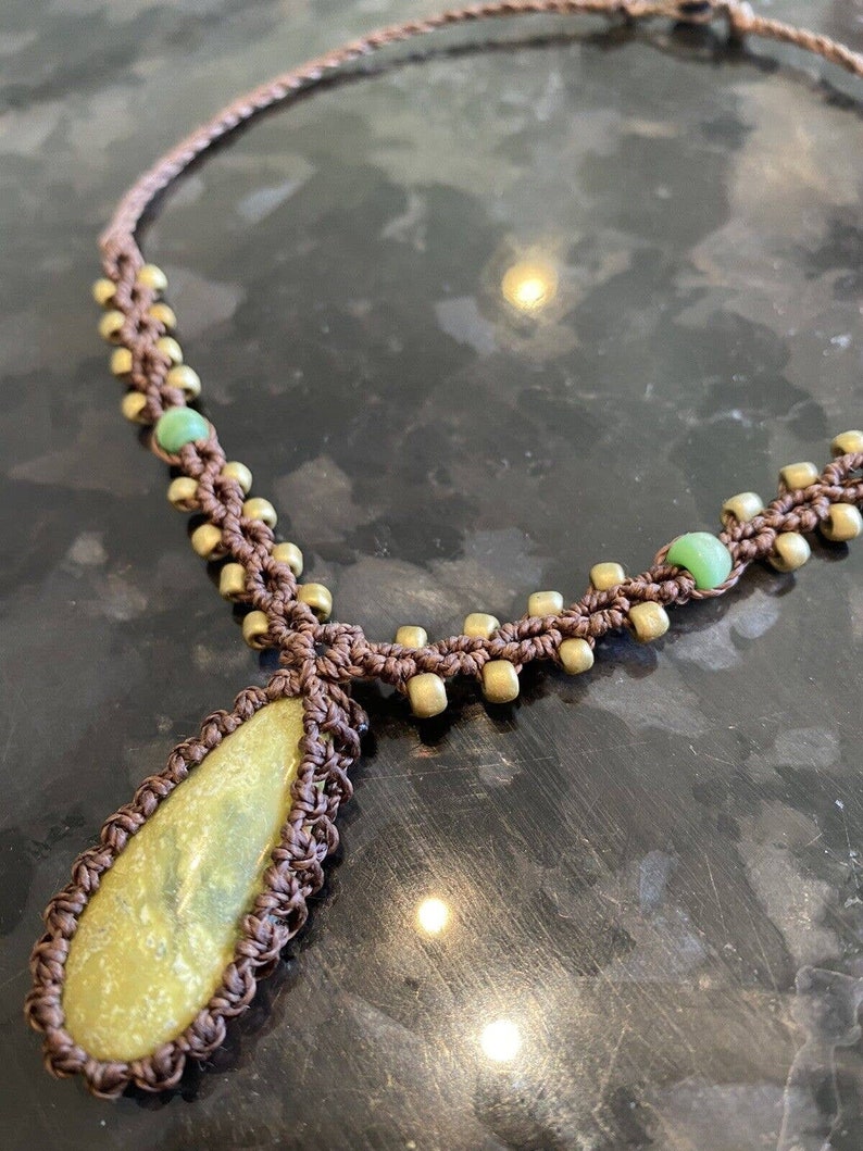 May include: A brown macrame necklace with a teardrop-shaped green stone pendant and gold beads.