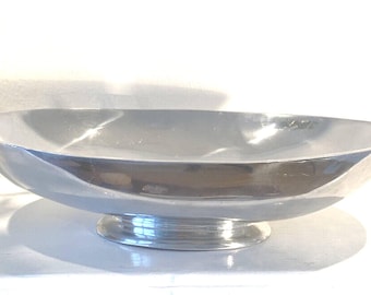 May include: A silver-colored, oval-shaped serving bowl with a pedestal base. The bowl has a smooth, reflective surface and is designed for displaying fruit or other decorative items. The pedestal base provides stability and adds to the bowl's elegant appearance.