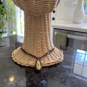 May include: A brown and green beaded necklace with a large teardrop-shaped yellow stone pendant. The necklace is displayed on a wicker mannequin head.
