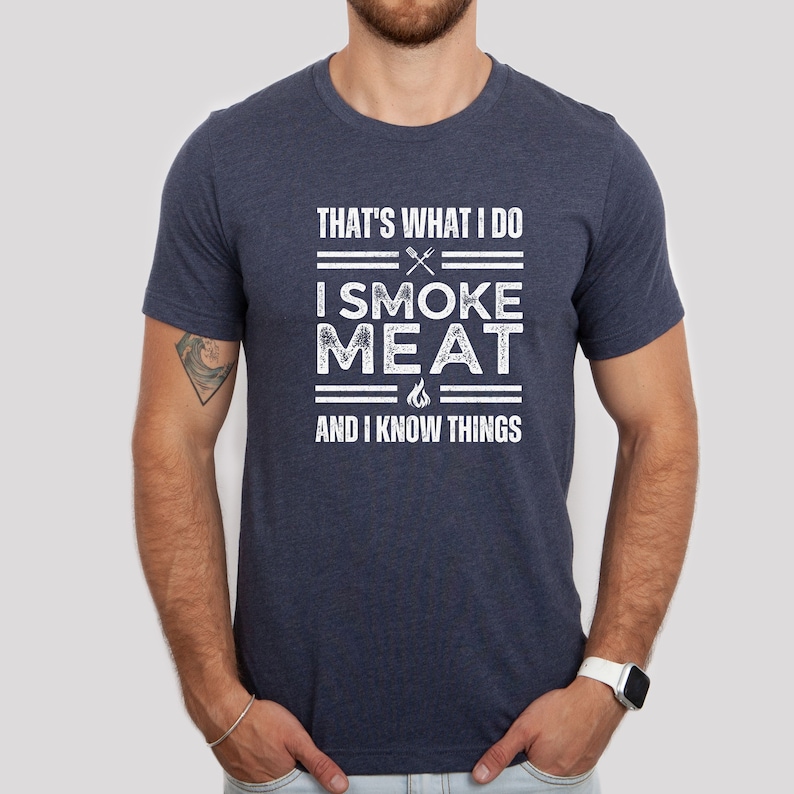 May include: A navy blue t-shirt with a white distressed graphic that reads "That's what I do I smoke meat and I know things".