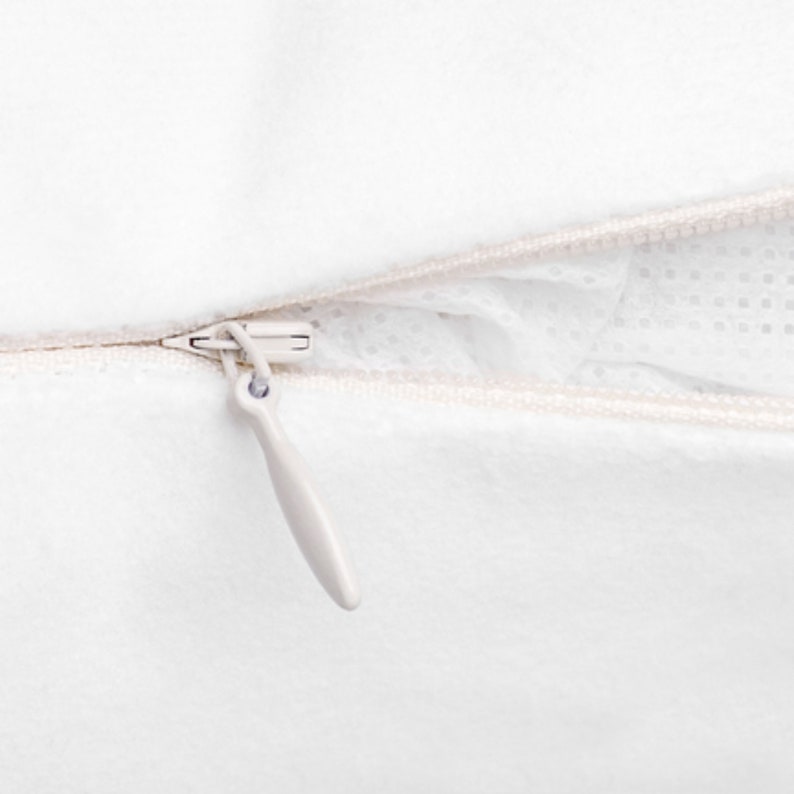 May include: Close-up of a white pillowcase with a beige zipper. The zipper is partially open, revealing the white interior of the pillow. The zipper pull is a light beige color.