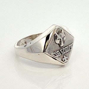 May include: A silver ring with a diamond-shaped design featuring a wolf head and the words "Cub Scouts".