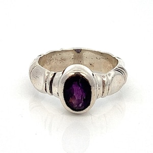 May include: A silver ring with a purple amethyst gemstone set in a bezel setting. The band is textured with a series of raised lines.