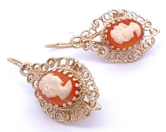 May include: A pair of gold filigree earrings with cameo insets. The cameos are oval shaped and feature a white cameo profile against a reddish-orange background.