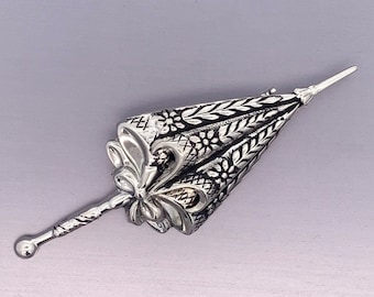 May include: A silver-toned brooch in the shape of a detailed, ornate umbrella with a floral design.