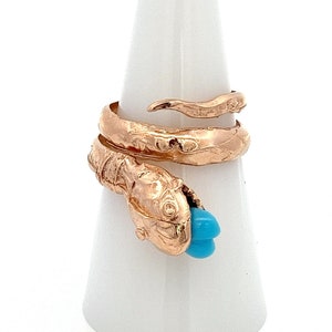 May include: A gold-toned snake ring with turquoise stones. The snake is coiled around the ring band and has a detailed, textured design.