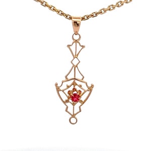 May include: A gold pendant necklace with a delicate, geometric design featuring a red gemstone in the center.