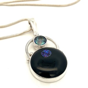 May include: A silver necklace with a black onyx pendant and a blue and green gemstone. The pendant is surrounded by a silver circle.