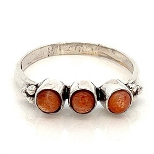 May include: A silver ring with three round orange stones set in the band.