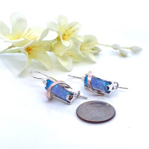 May include: A pair of silver earrings with a blue opal stone set in a copper wire design. The earrings are about the size of a US penny.
