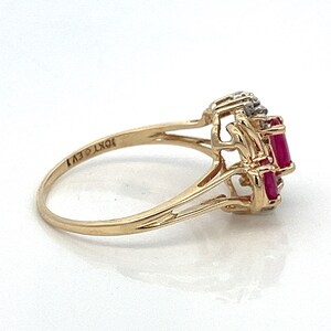 May include: A gold ring featuring three red ruby stones and small diamonds set in a delicate, intricate design. The ring is marked "10KT EV1" on the inside band.