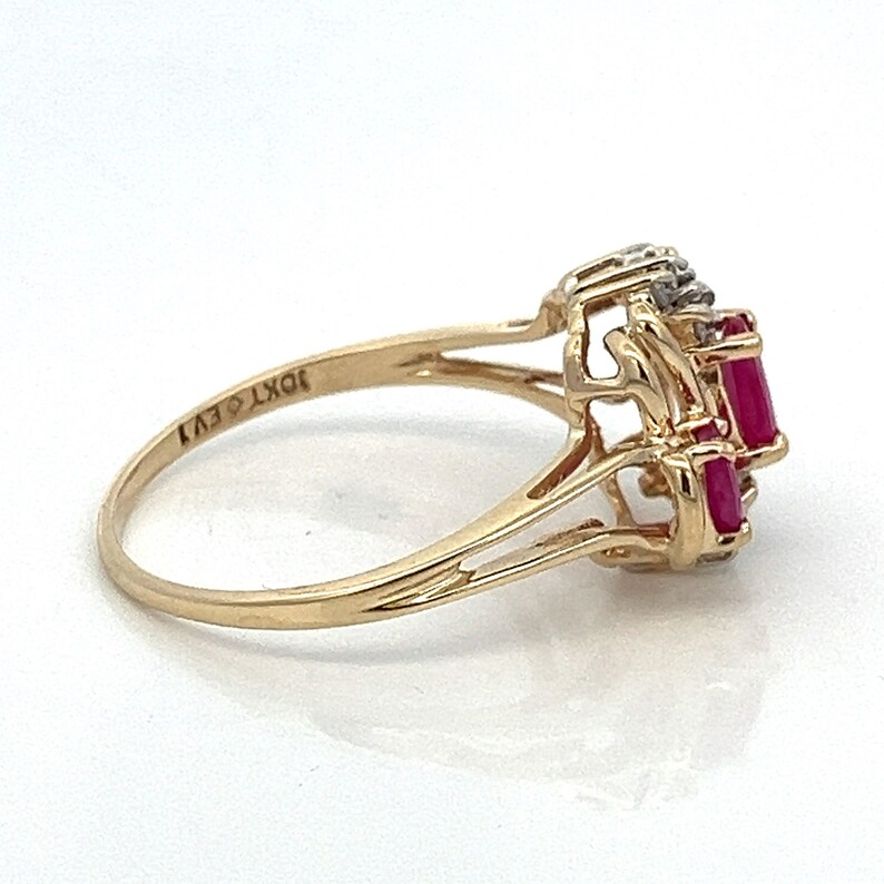 May include: A gold ring featuring three red ruby stones and small diamonds set in a delicate, intricate design. The ring is marked "10KT EV1" on the inside band.