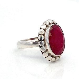 May include: A silver ring with a large, oval-shaped, deep red gemstone set in a beaded bezel.