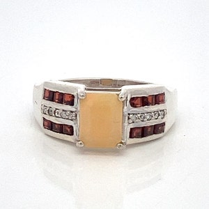 May include: A silver ring with a rectangular, light orange stone set in the center. The ring is accented with two rows of small, red gemstones and two rows of small, clear gemstones.