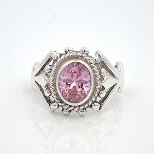 May include: A silver ring with a pink oval gemstone set in a decorative silver bezel. The ring has a detailed design with small silver beads and a rope-like border.