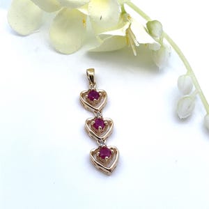 May include: Gold pendant necklace with three ruby hearts. Each heart has a small diamond accent.