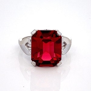 May include: A silver ring with a large, red, emerald-cut gemstone.