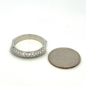 May include: A silver band ring with a row of small diamonds set in a curved design. The ring is shown next to a US quarter for size comparison.