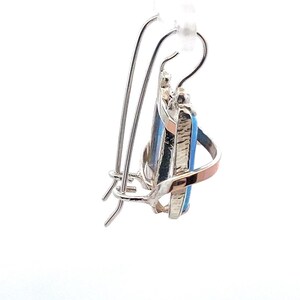 May include: Silver and gold tone earrings with a blue and black gemstone. The earrings have a hook closure.