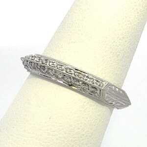 May include: A silver band ring with a diamond-encrusted design. The ring has a pointed edge and a delicate floral pattern.