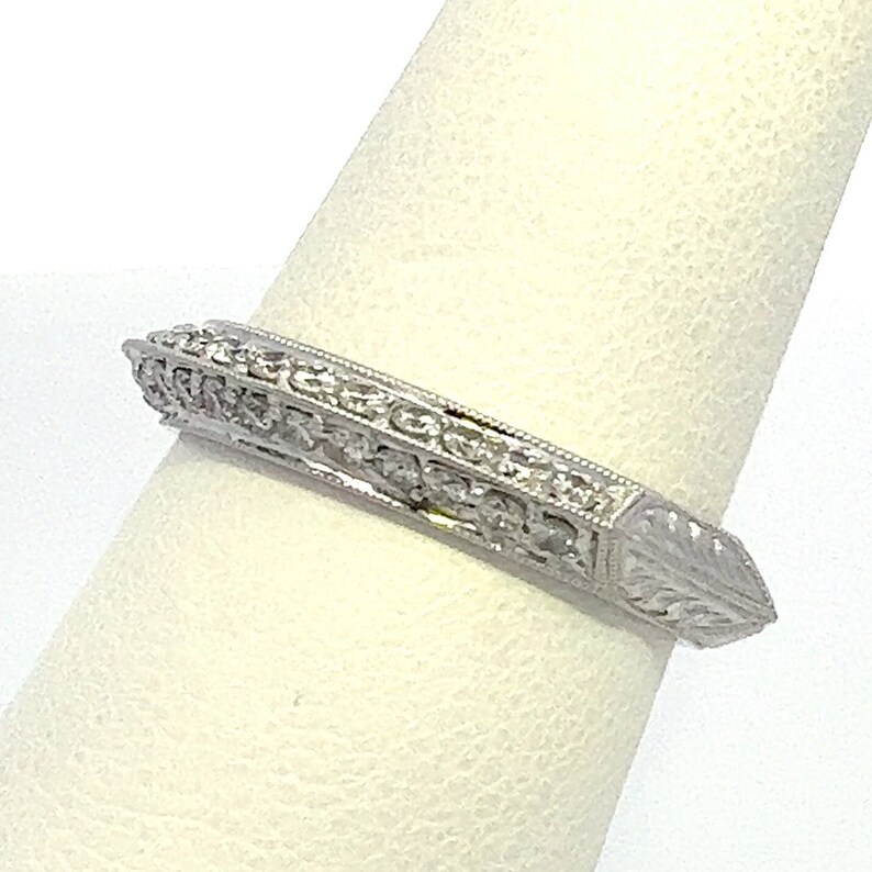 May include: A silver band ring with a diamond-encrusted design. The ring has a pointed edge and a delicate floral pattern.