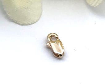 May include: A small, gold-colored lobster clasp, designed for jewelry making. The clasp has a rounded top with a small loop and a lever-operated closure. The metal has a polished finish, reflecting light.