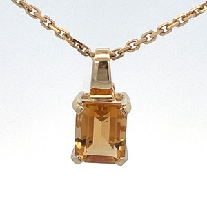 May include: A gold chain necklace with a pendant featuring a large, rectangular, orange citrine gemstone.