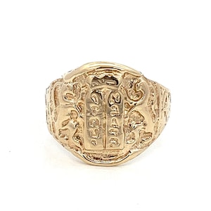 May include: A gold ring with intricate carvings and a raised inscription. The inscription is in a foreign language and appears to be a religious symbol.