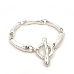 May include: A silver bracelet with a toggle clasp. The bracelet is made of smooth, rounded links.