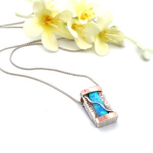 May include: A silver chain necklace with a rectangular pendant featuring a blue opal stone set in a silver and rose gold frame.