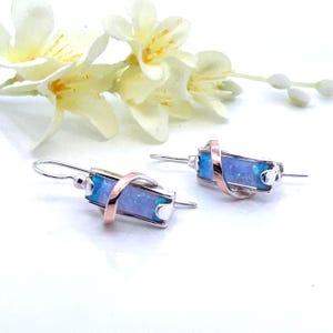 May include: A pair of silver earrings with a blue opal stone set in a twisted silver and rose gold band.