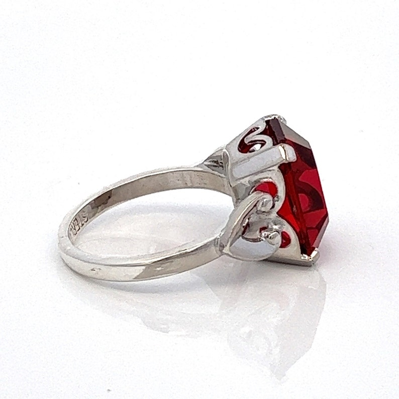 May include: A silver ring featuring a large, red, faceted gemstone set in an ornate, decorative setting.