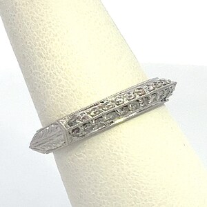 May include: A silver band ring with a pointed edge and a row of small diamonds set in the band.