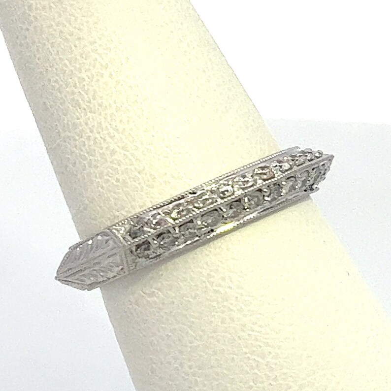 May include: A silver band ring with a pointed edge and a row of small diamonds set in the band.