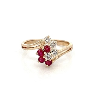 May include: A gold ring with a cluster of red rubies and white diamonds set in a swirling design.