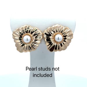 May include: A pair of gold-colored flower-shaped earrings with a white pearl center. The earrings are displayed on a white stand. The text "Pearl studs not included" is visible below the earrings.