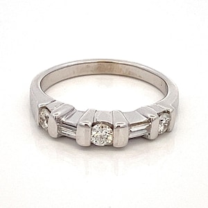 May include: A silver band ring with five diamonds. The centre diamond is round and the two diamonds on either side are baguette-shaped.