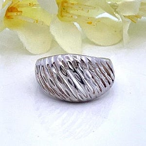 May include: A silver ring with a textured, ridged design. The ring is a simple, modern style.